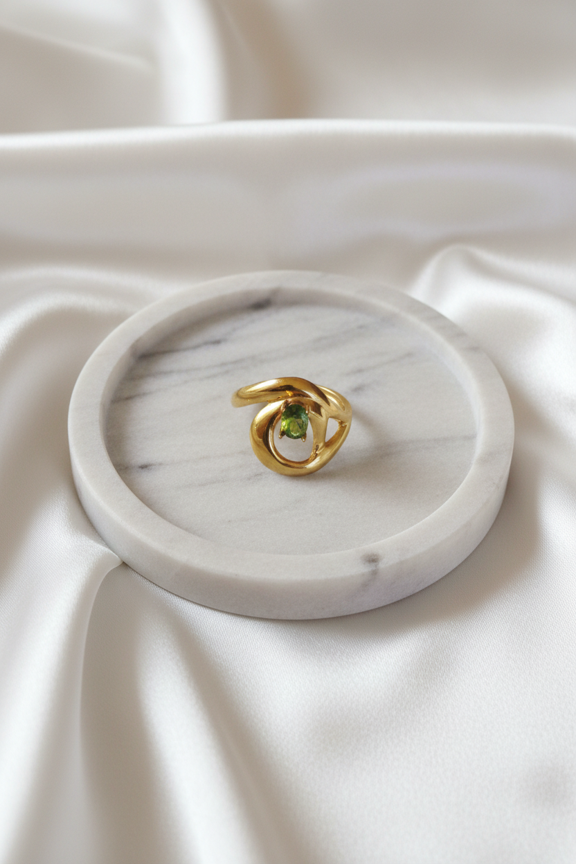 Bague tourbillon dorée pierre verte sur plateau marbré