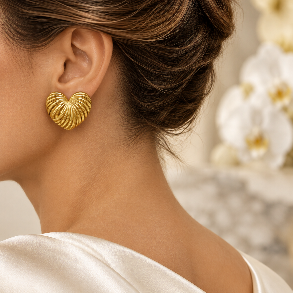 Boucle cœur doré strié portée à l’oreille gauche dans le même décor élégant