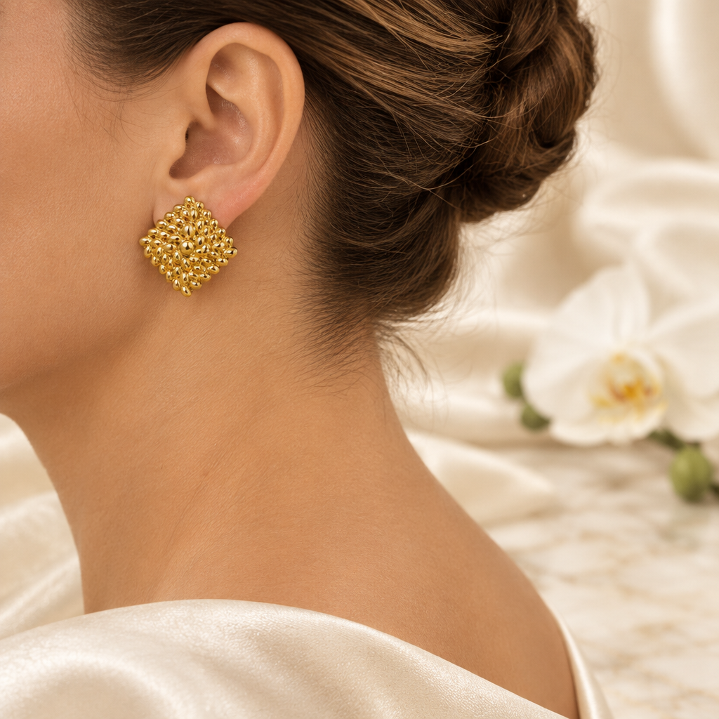 Boucle dorée texturée portée à l’oreille gauche dans le même décor élégant