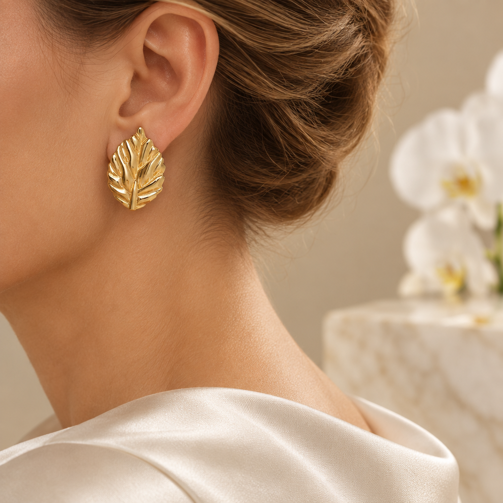 Boucle feuille dorée portée à l’oreille gauche dans le même décor élégant