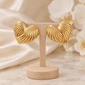 Boucles cœurs dorés striés sur un présentoir en bois dans un décor chic