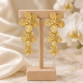 Boucles dorées à trois fleurs sur un présentoir en bois dans un décor chic