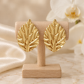Boucles feuilles dorées sur un présentoir en bois dans un décor chic