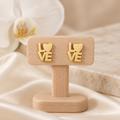 Boucles LOVE dorées sur un présentoir en bois dans un décor chic